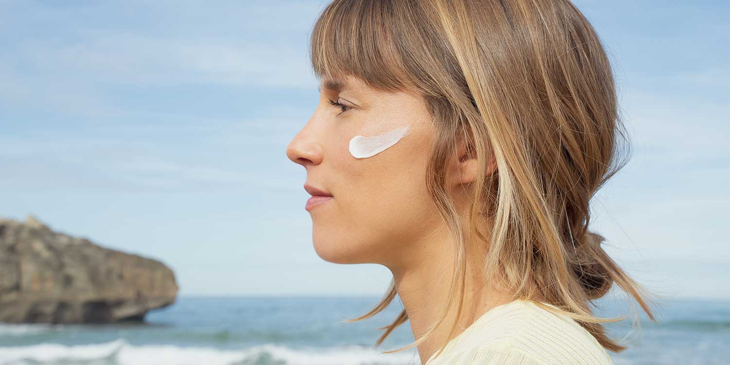 femme au bord de l'océan qui à de la crème sur la joue